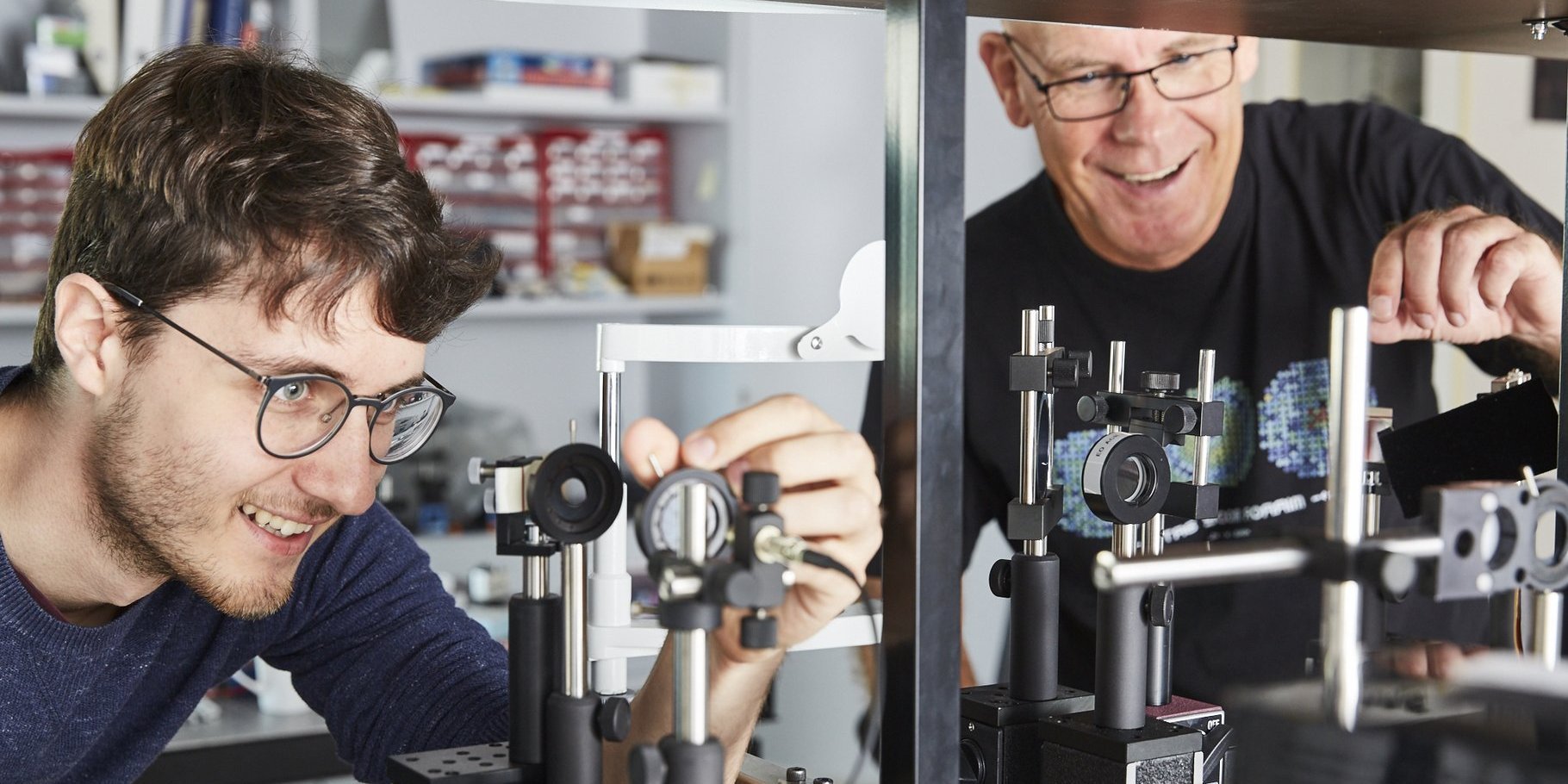 Prof. Blendowske und ein Student stehen im Optiklabor an einem Versuchsaufbau und sind mit Spaß an der Arbeit, denn beide lachen fröhlich. Sie justieren Blenden in einem Strahlengang.
