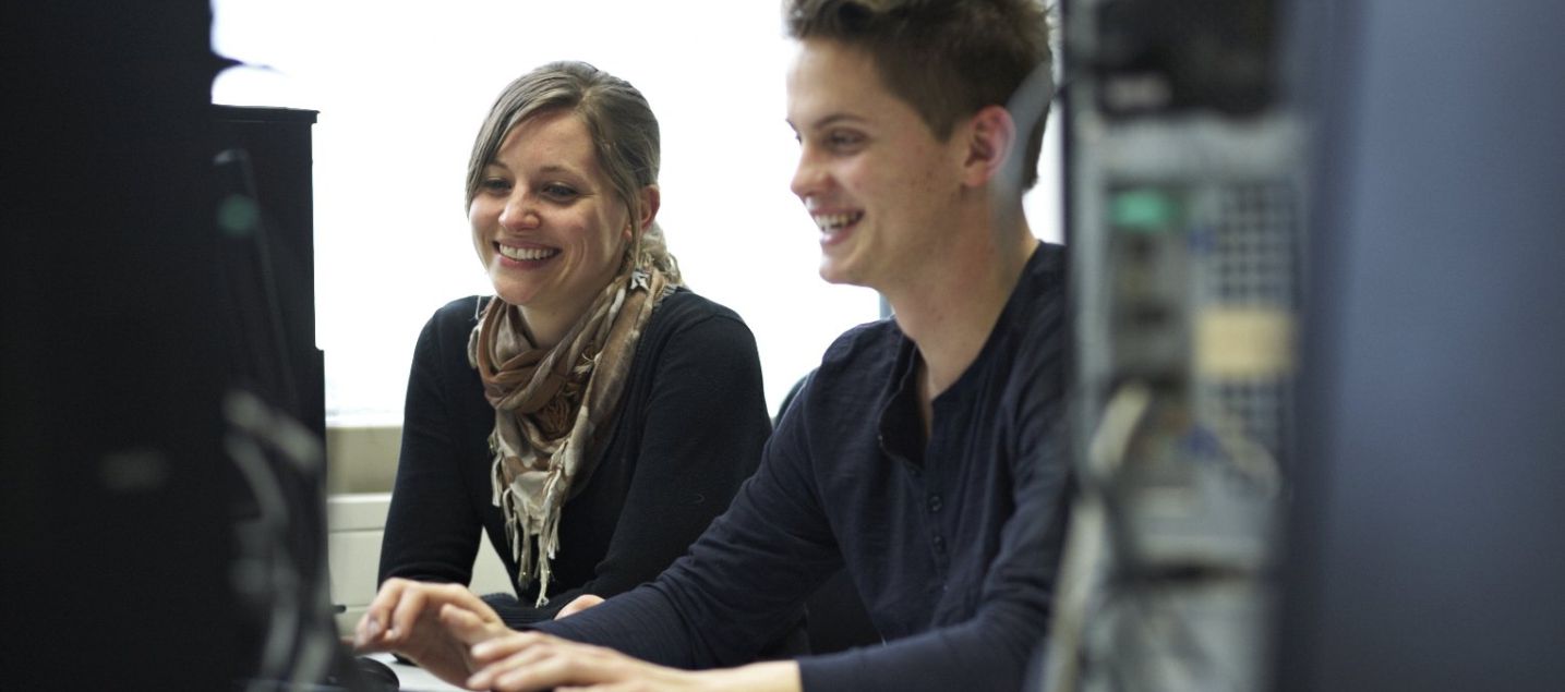 Ein Student und eine Studentin sitzen gemeinsam lachend an einem Rechner im Mathelabor