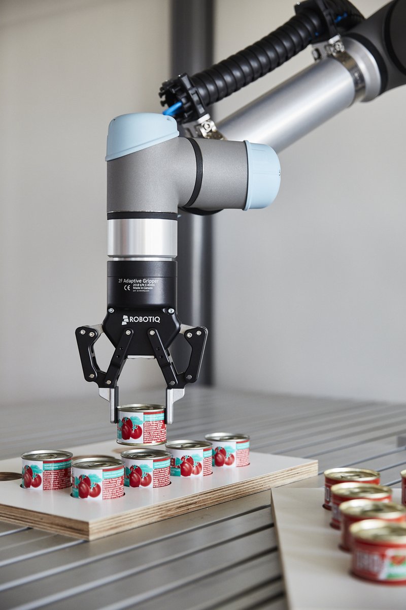 Ein Roboterarm greift nach einer kleinen Konservendose, um sie von einem Tablett auf ein anderes zu setzen.