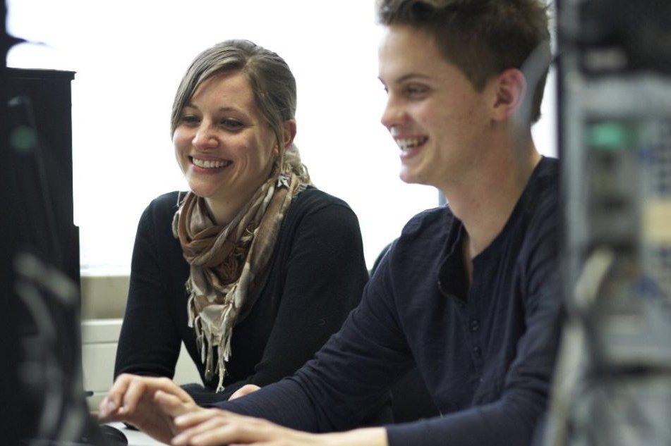 Ein Student und eine Studentin sitzen gemeinsam lachend an einem Rechner im Mathelabor
