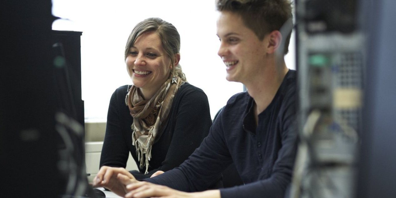 Ein Student und eine Studentin sitzen gemeinsam lachend an einem Rechner im Mathelabor