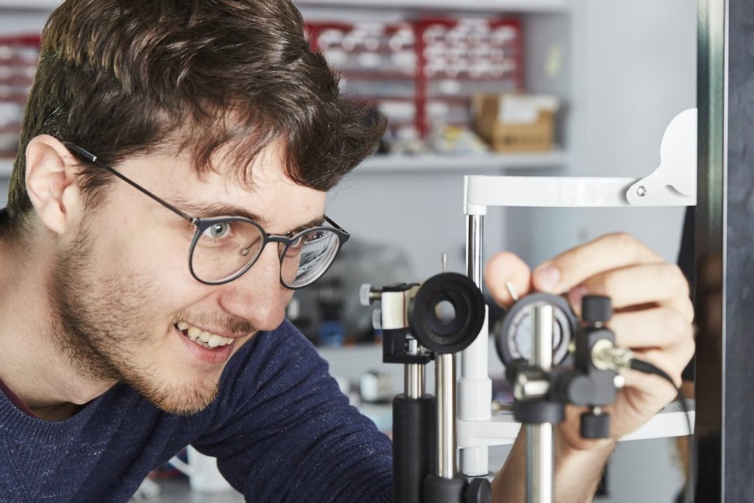 Prof. Blendowske und ein Student stehen im Optiklabor an einem Versuchsaufbau und sind mit Spaß an der Arbeit, denn beide lachen fröhlich. Sie justieren Blenden in einem Strahlengang.